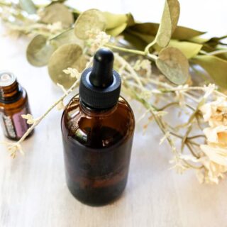 A homemade facial oil with an essential oil bottle and dried flowers in the background.