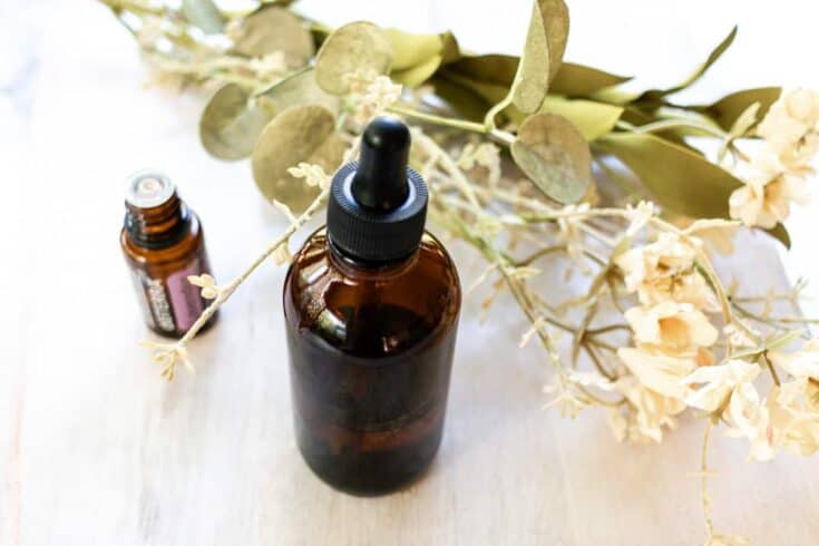 A homemade facial oil with an essential oil bottle and dried flowers in the background.