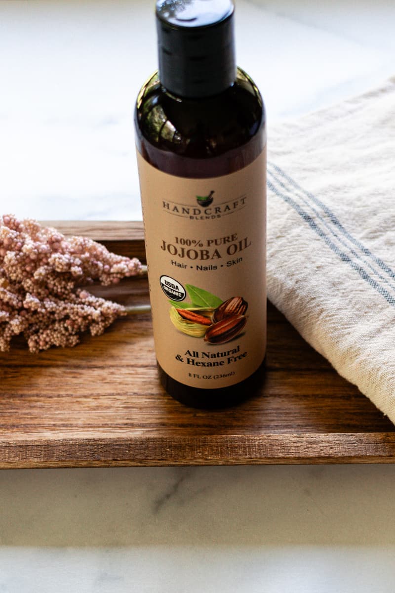 Jojoba oil sitting on a wooden tray. 