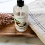 A bottle of fractionated coconut oil on a wooden tray on a white marble vanity.