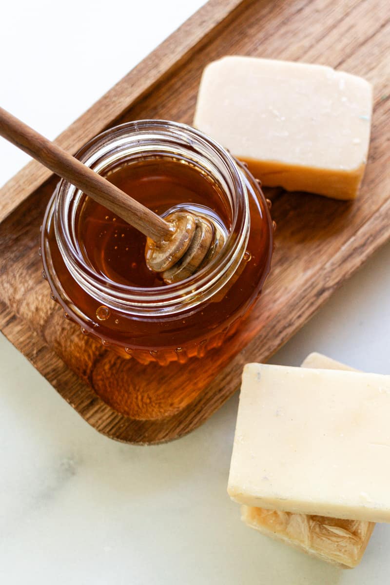 Dipping a honey comb into a jar of honey to be used in soap making. Several soap bars are placed around it. 