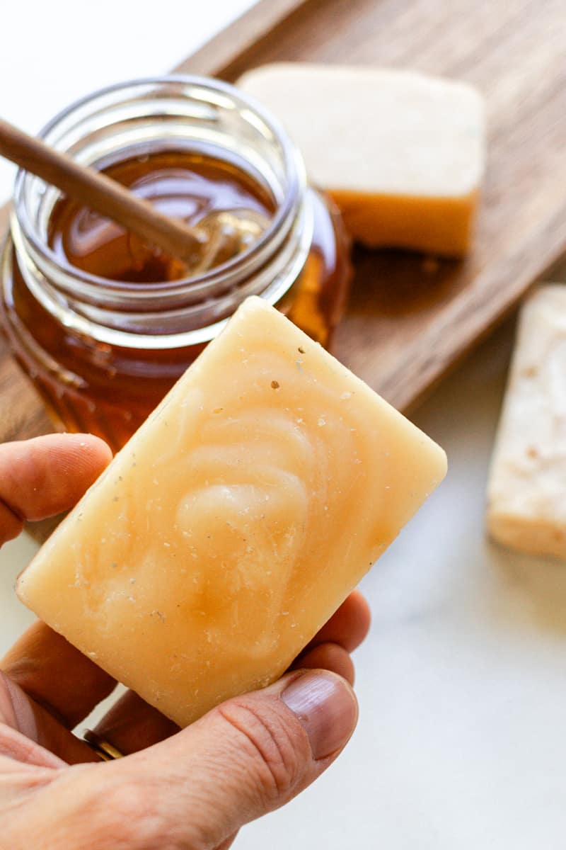 Holding a bar of honey soap with a glass of honey in the background.