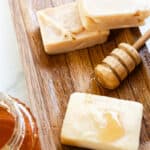 Three soap bars made with honey on a wooden curing rack with a honey comb next to it.