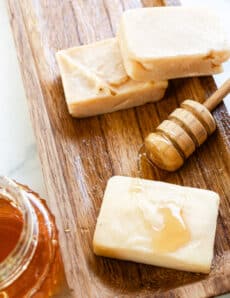 Three soap bars made with honey on a wooden curing rack with a honey comb next to it.