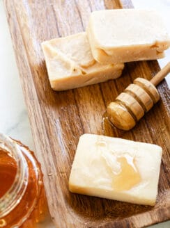 Three soap bars made with honey on a wooden curing rack with a honey comb next to it.