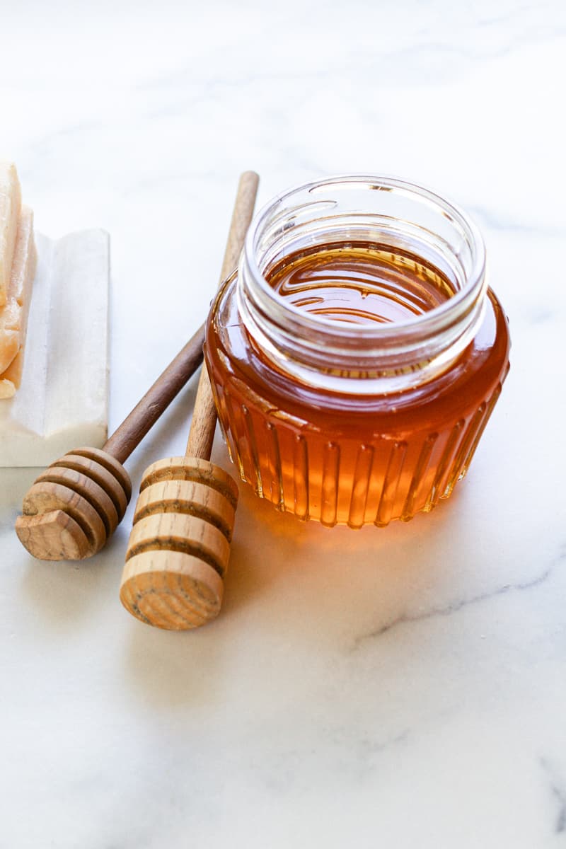 A jar of local honey with two honey combs on a white marble table. 