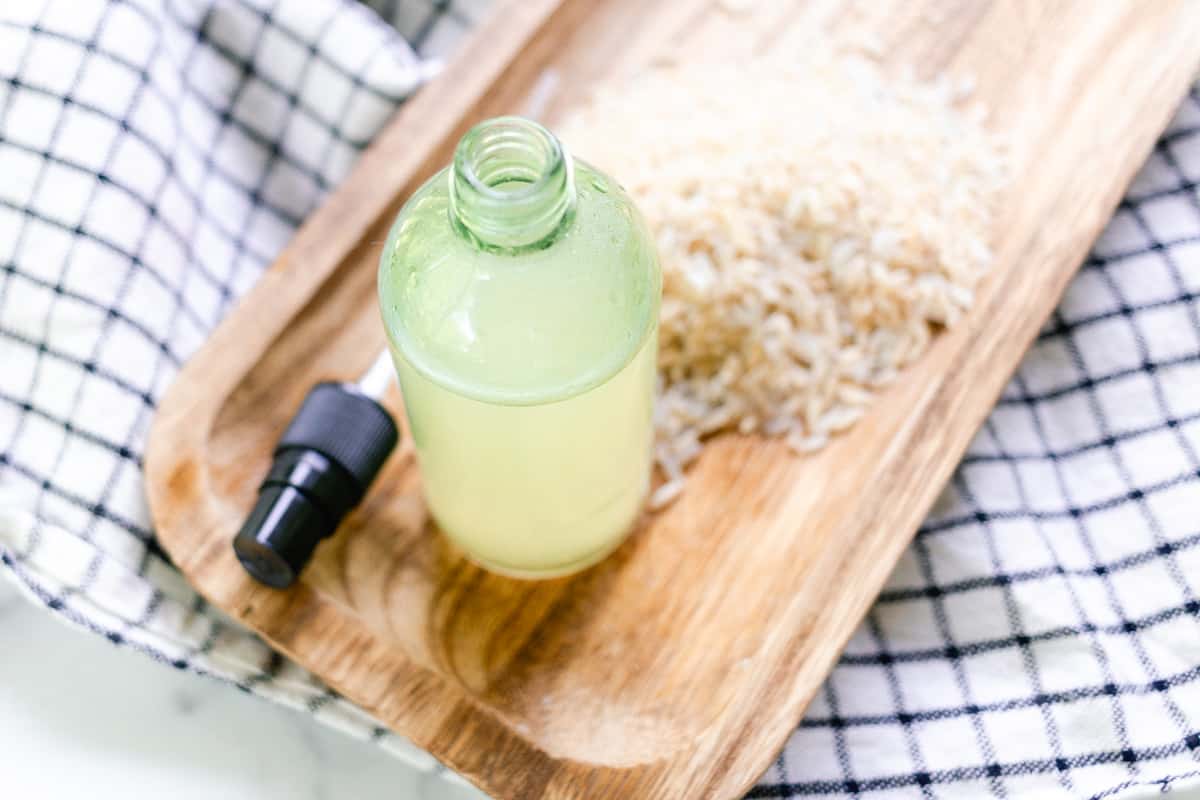A bottle of homemade rice water for the hair with the lid off next to it and a small pile of brown rice.