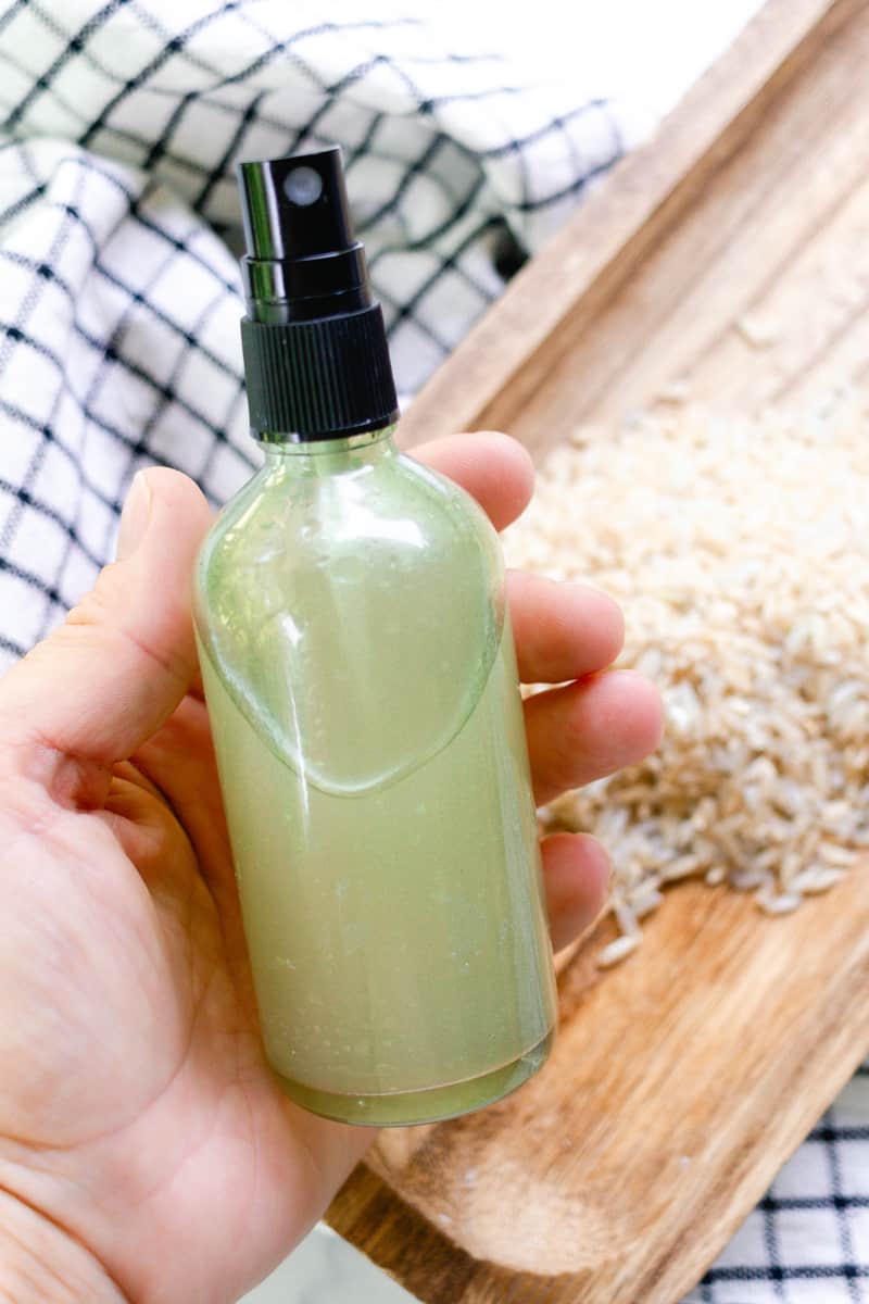 Holding a spray bottle of rice water for hair.