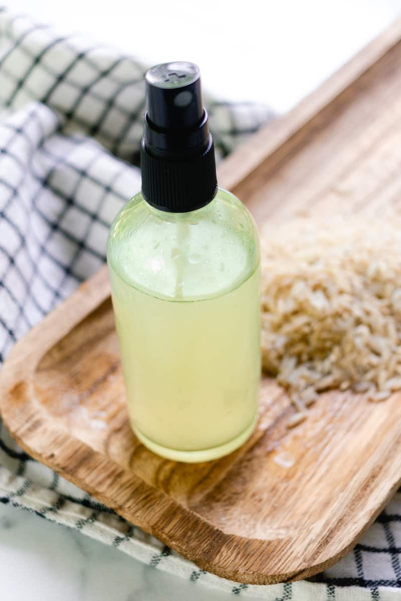 A spray bottle of homemade rice water for the hair on a wooden tray.