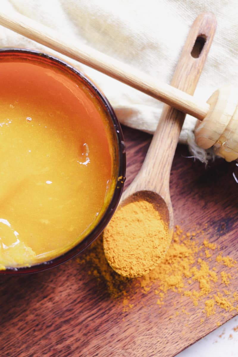 Freshly made sea moss face mask on a wooden board with a spoon full of turmeric powder next to it.