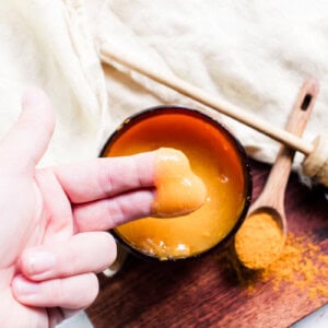 Using the finger tips to scoop up a small amount of the face mask out of the container.