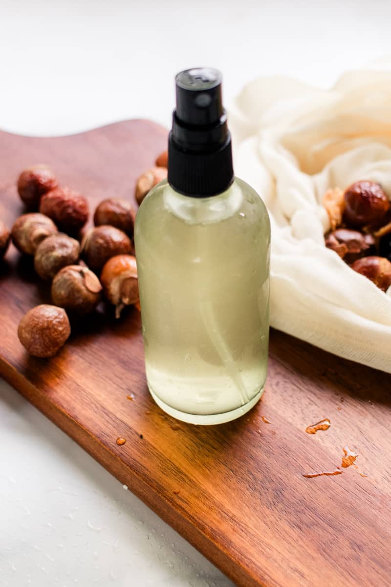 A homemade soap nut shampoo in a spray bottle with soap nuts surrounding it.