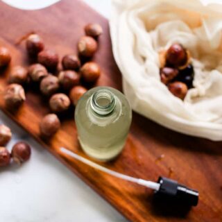 A homemade soap nut shampoo on a wooden board with soap nuts around it.