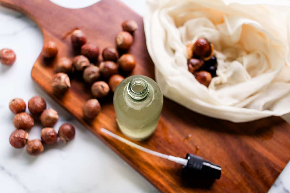 Homemade soap nut shampoo on a wooden board that is sitting on a white vanity.