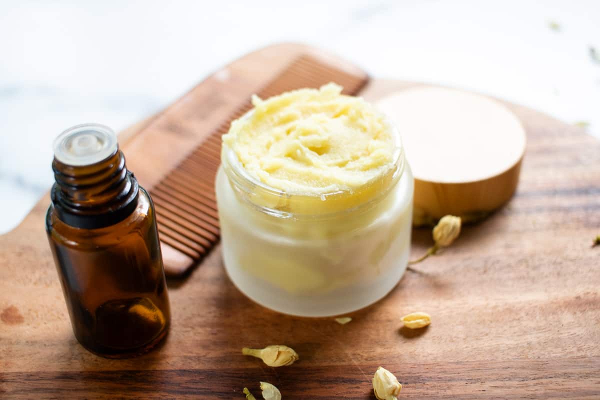 Homemade beard butter cooling off completely in a small container with a beard comb and EO bottle next to it.