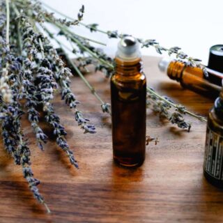 DIY lip oil in a 10mL roller bottle on a wooden staging tray with lavender springs.