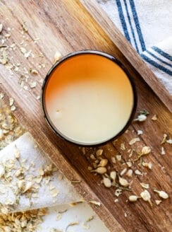 All natural tallow balm recipe setting up in a large storage container on a marble vanity with dried flowers.