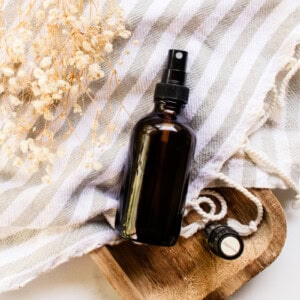 DIY hair perfume in an amber spray bottle on a grey and white striped tea towel.