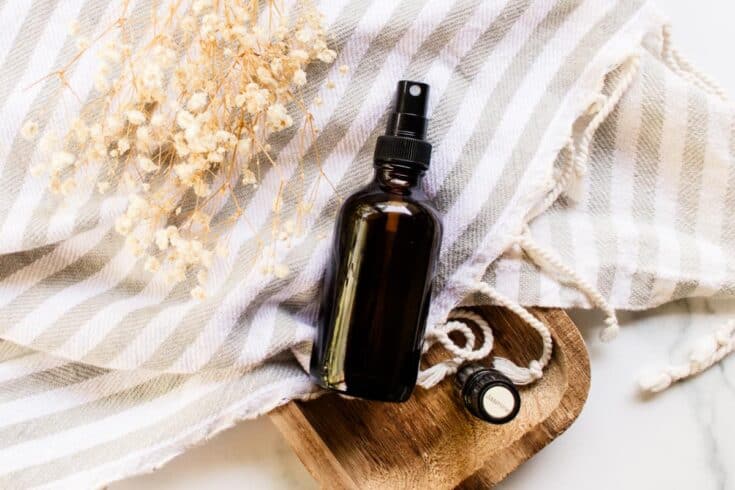 DIY hair perfume in an amber spray bottle on a grey and white striped tea towel.