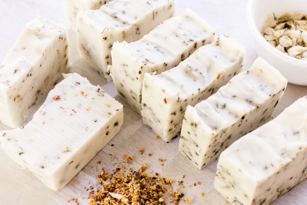 Homemade herbal soap bars curing on a white table with dried flower petals all around it.