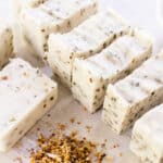 Homemade herbal soap bars curing on a white table with dried flower petals all around it.