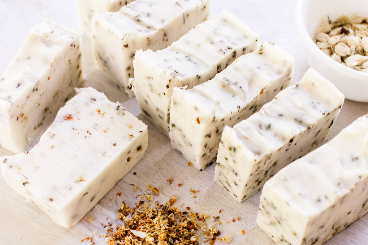 Homemade herbal soap bars curing on a white table with dried flower petals all around it.