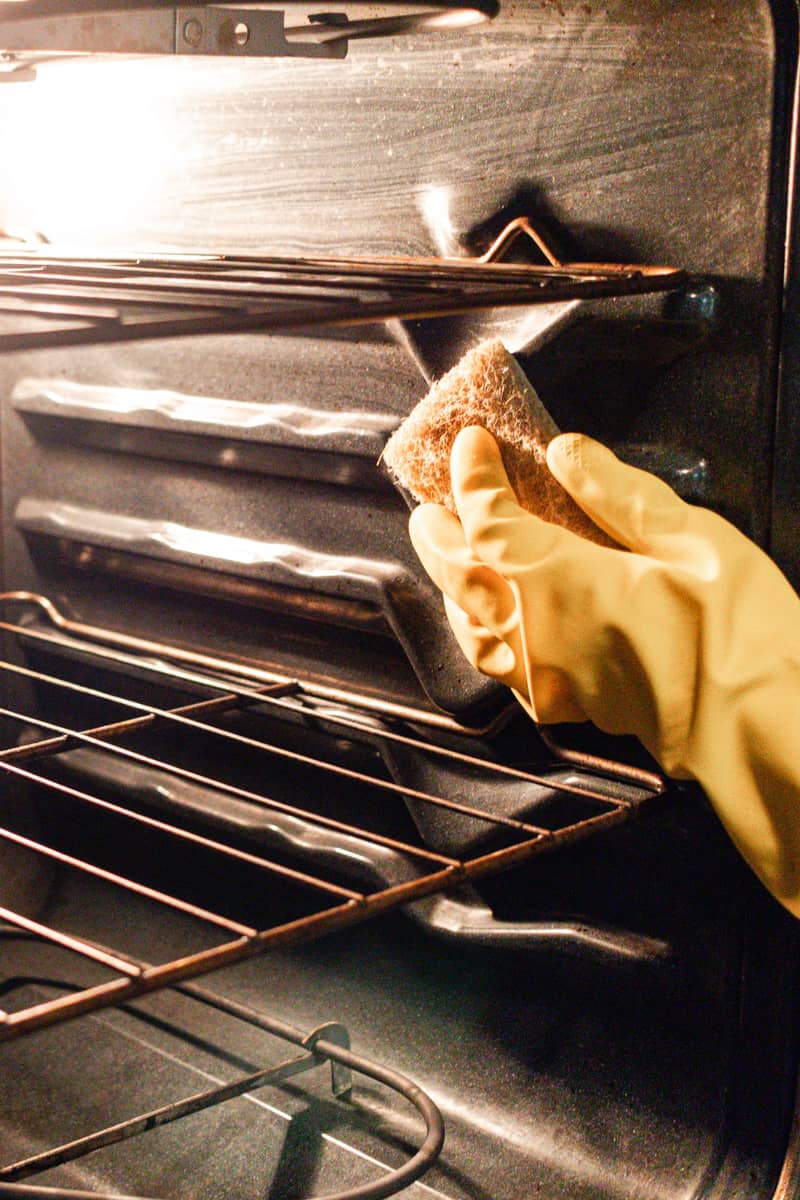Using a coarse brush to scrub the sides of an oven free of grease after loosening it with steam.