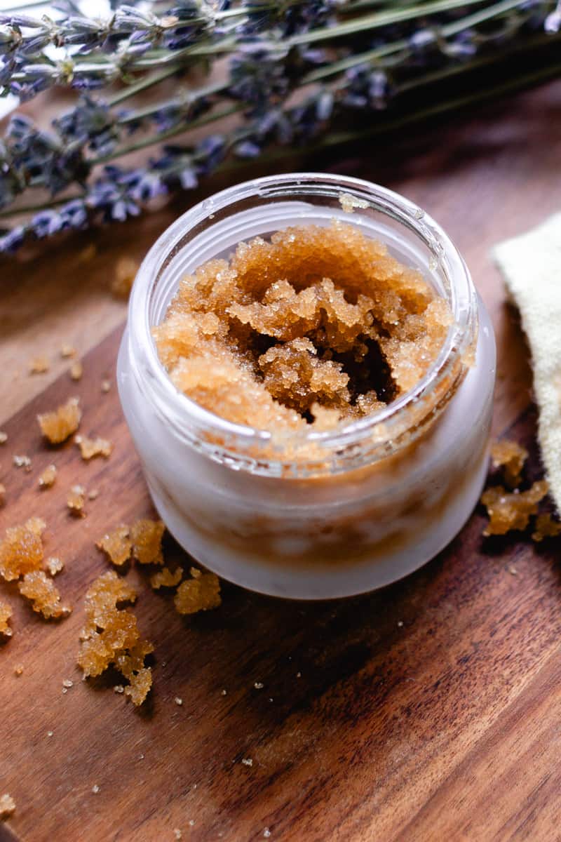 A glass jar of underarm exfoliator with lavender sprigs in the background