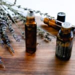 DIY lip oil in a glass roller bottle on a wooden staging shelf with lavender sprigs in the background.