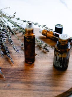 DIY lip oil in a glass roller bottle on a wooden staging shelf with lavender sprigs in the background.