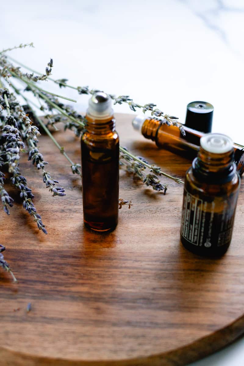 DIY lip oil in a glass roller bottle on a wooden staging shelf with lavender sprigs in the background.