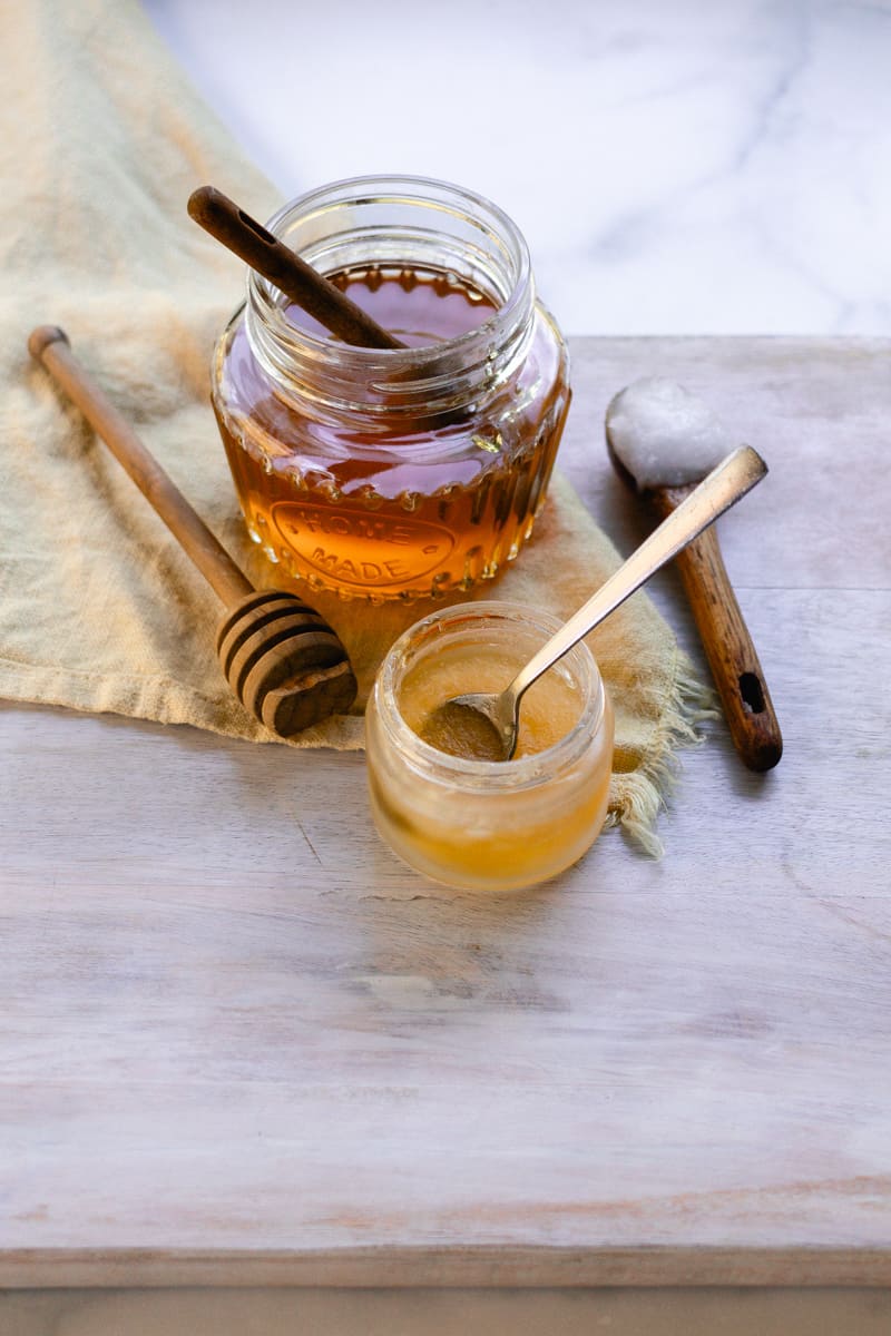 A homemade lip mask on a wooden table with honey and coconut oil in the background. 