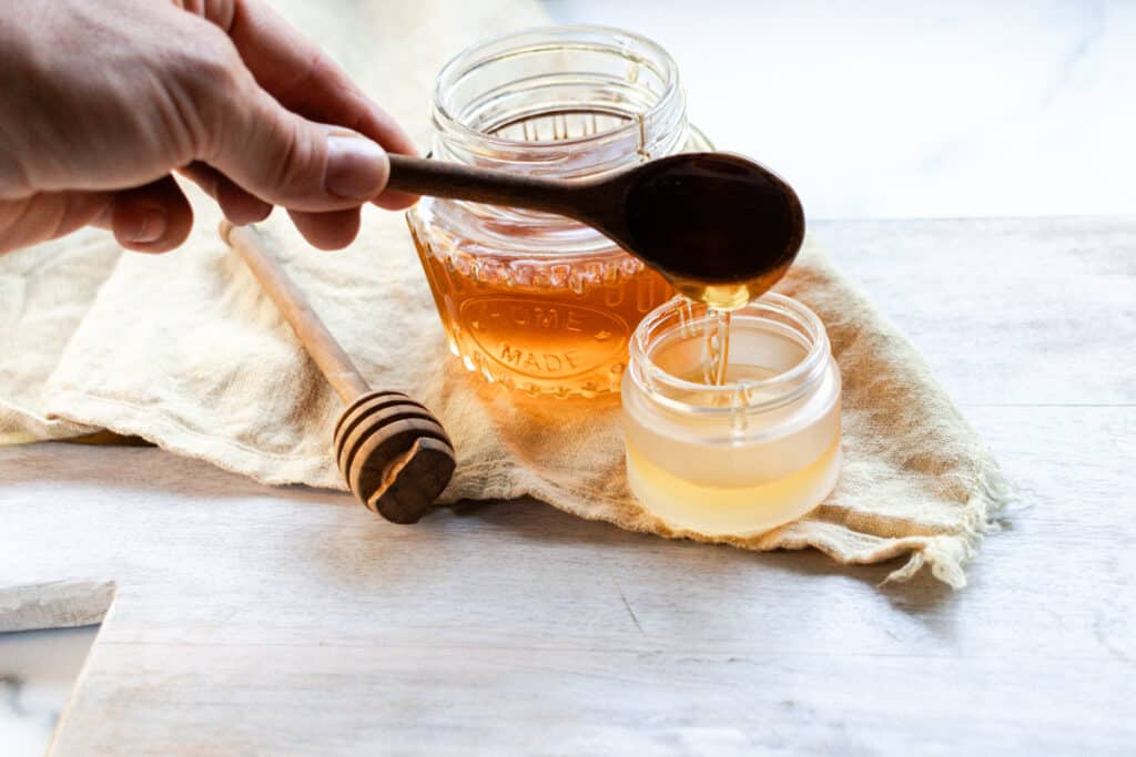 Adding honey to a container to make the lip mask.