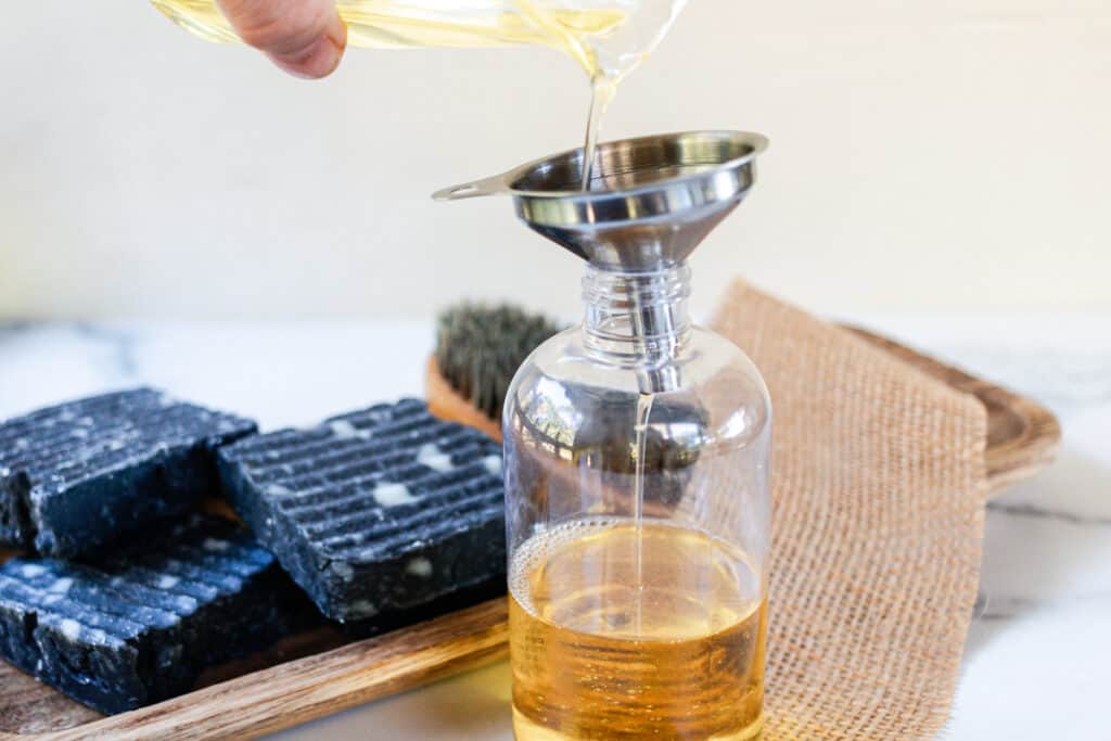 Pouring the pre shave oil into a storage bottle using a funnel to prevent spills.
