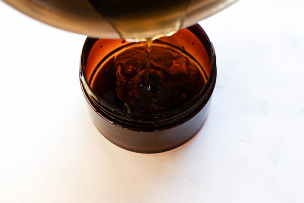 Pouring the melted foot mask ingredients out of the saucepan into the container.