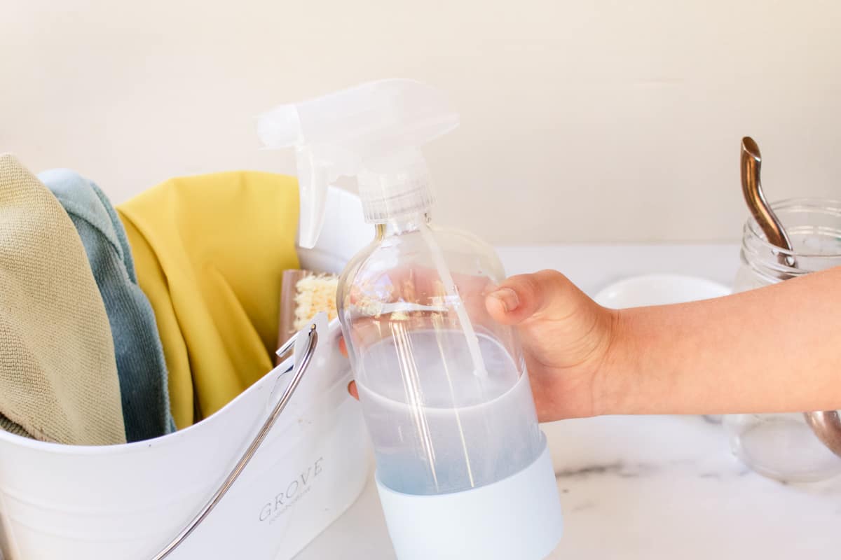 Shaking a bottle of mold cleaner to spray on tile grout.