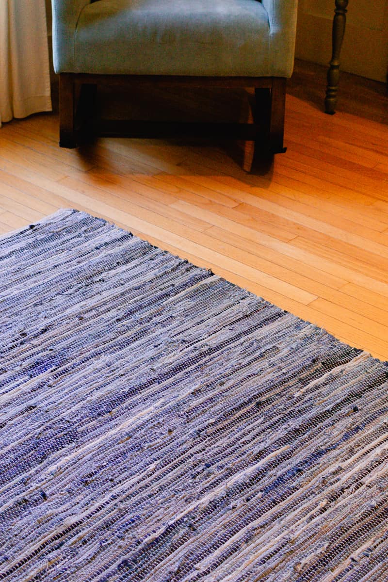 A close up shot of a braided rug with a rocker in the background.