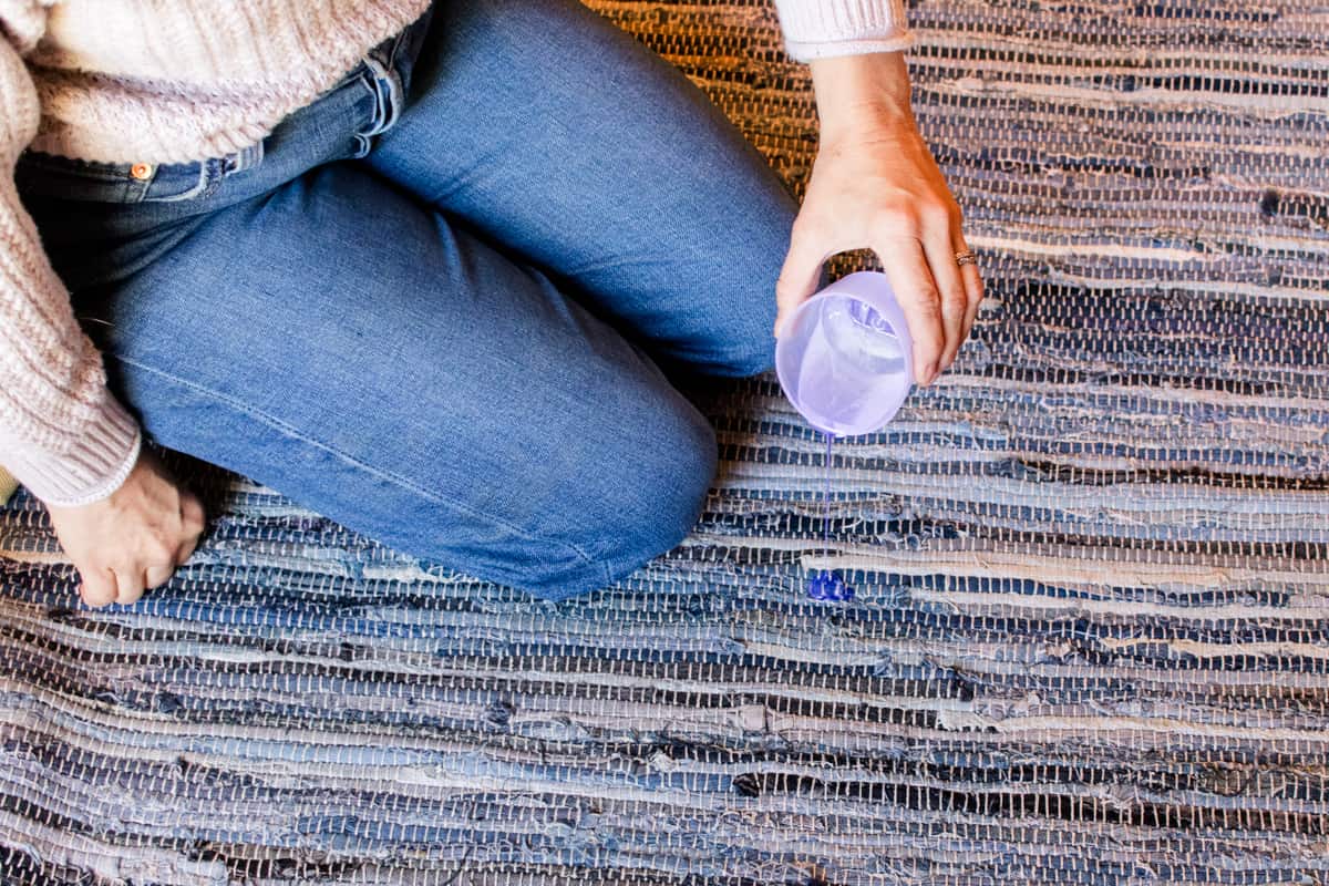 Pouring a gentle detergent onto a small stain in the middle of the rug.