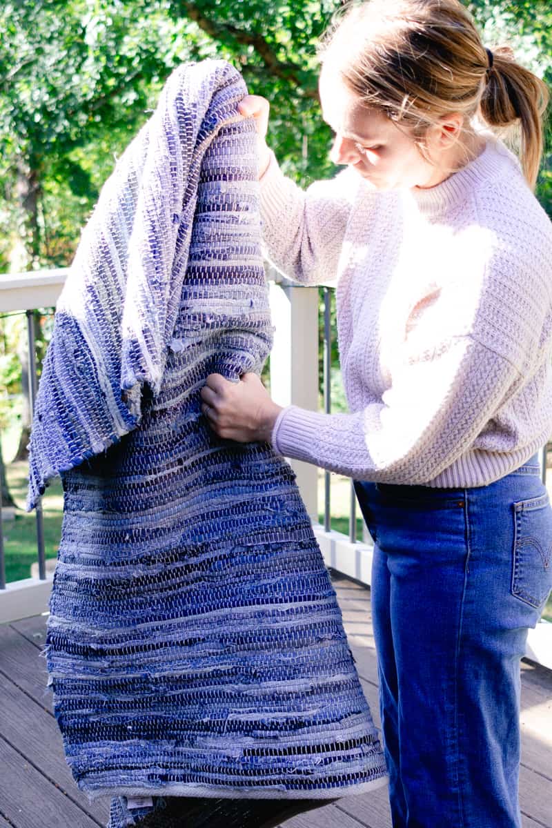 Shaking the dust out of a braided rug outside.