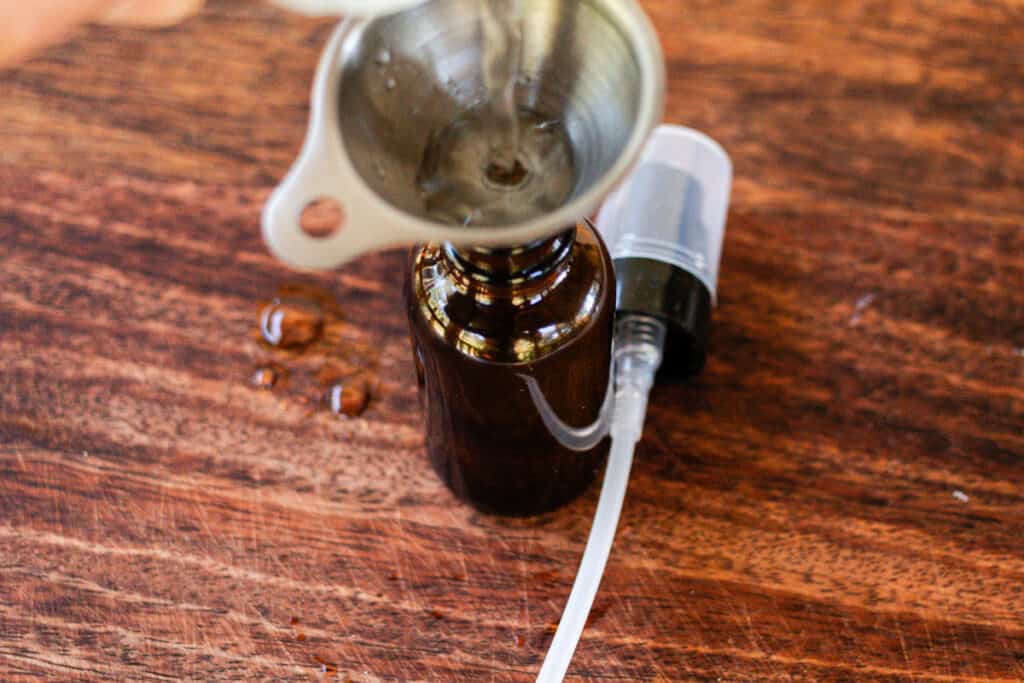 Pouring the ingredients into a spray bottle using a funnel to prevent spills.