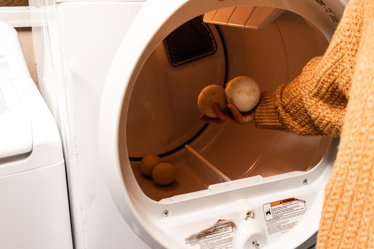 Placing wool dryer balls into a dryer before adding the clean clothes from the wash.