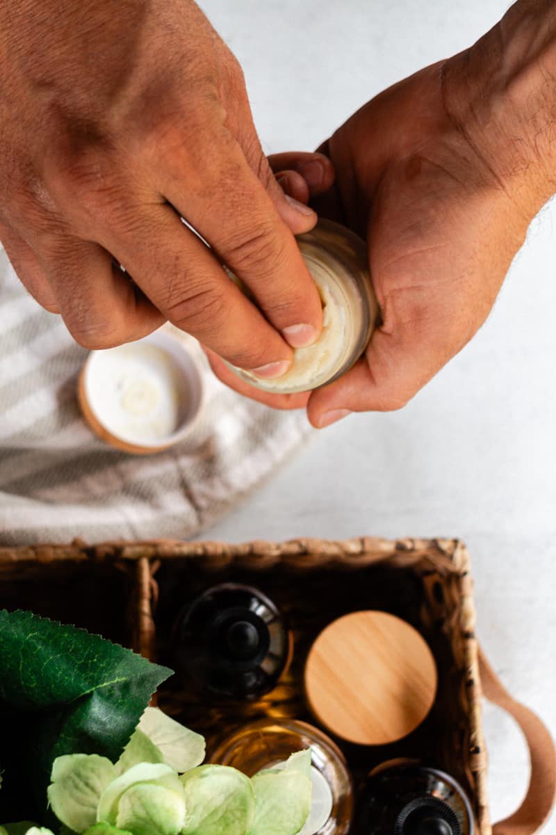 Using 2 fingers to swipe a little beard balm out of the container over a white vanity.