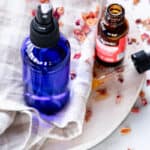A hydrating face mist in a blue spray bottle on a white marble vanity.