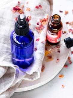 A hydrating face mist in a blue spray bottle on a white marble vanity.