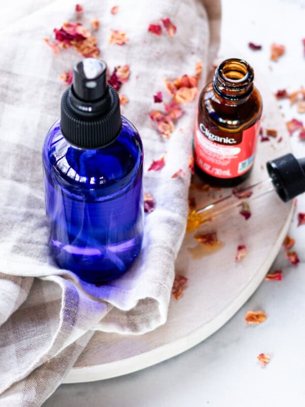 A hydrating face mist in a blue spray bottle on a white marble vanity.