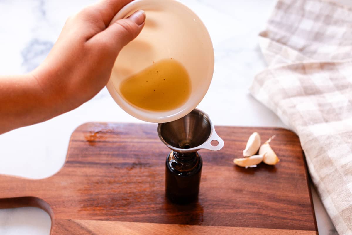 Using a funnel to pour the olive oil into the glass storage container.