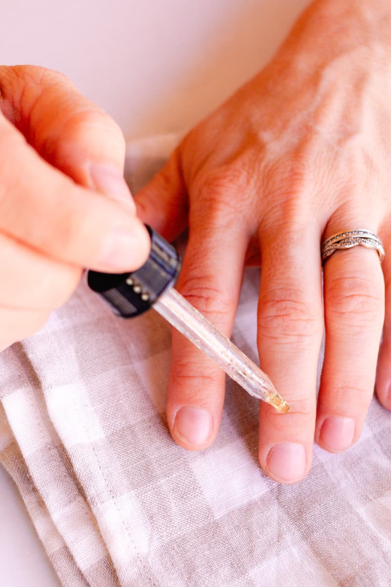 Using a dropper to apply the nail growth serum to the base of the nails.