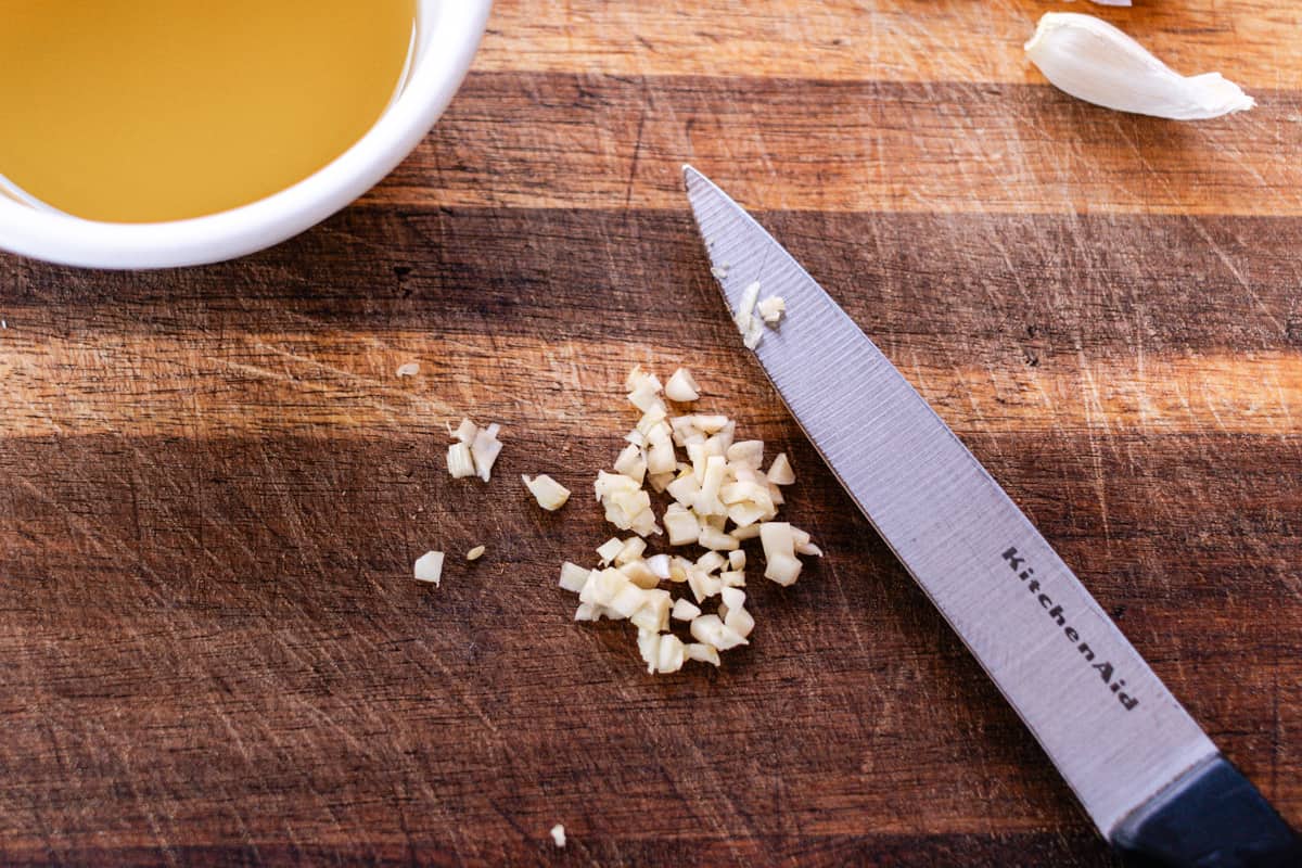 Dicing up a clove of garlic on a wooden cutting board.