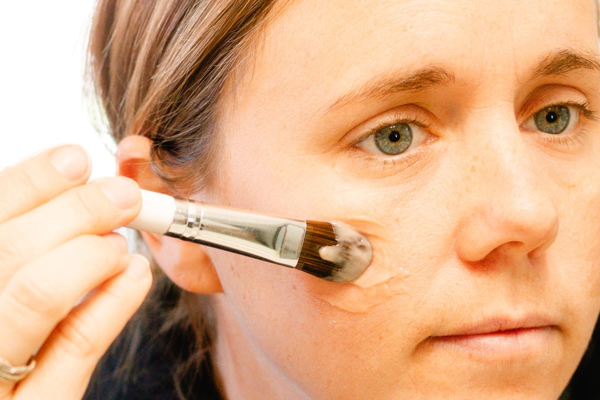 Using a foundation brush to apply a homemade liquid foundation to my cheek bone.