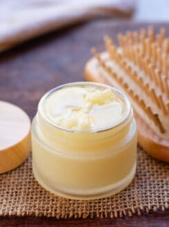 Small jar of DIY hair pomade with a wooden brush in the background.